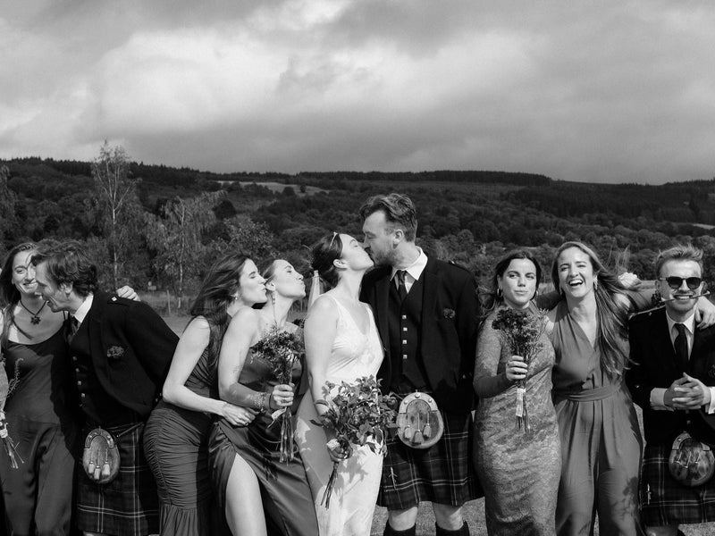 Bride and groom kissing with bridal party in kilts and mismatched dresses, Scottish Highlands wedding