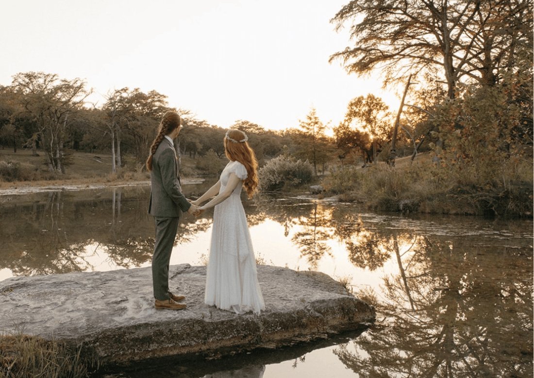 Bride in a 1940s lace dress with a long tulle veil on a sunlit rock at sunset.