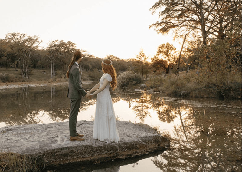 Bride in a 1940s lace dress with a long tulle veil on a sunlit rock at sunset.